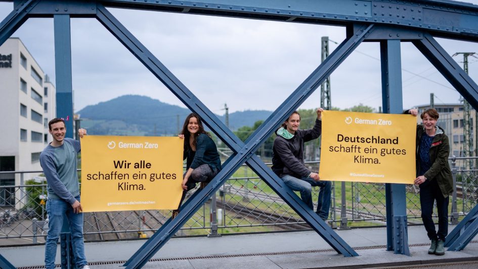 Vier Menschen mit gelben Bannern auf blauem Stahlgerüst